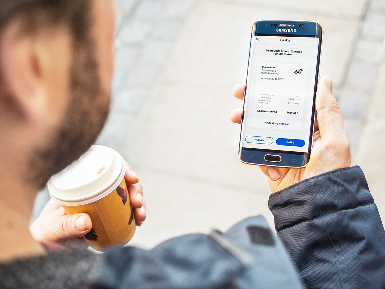 Mies kahvikuppi kädessä hyväksymässä laskua MobilePay sovelluksella