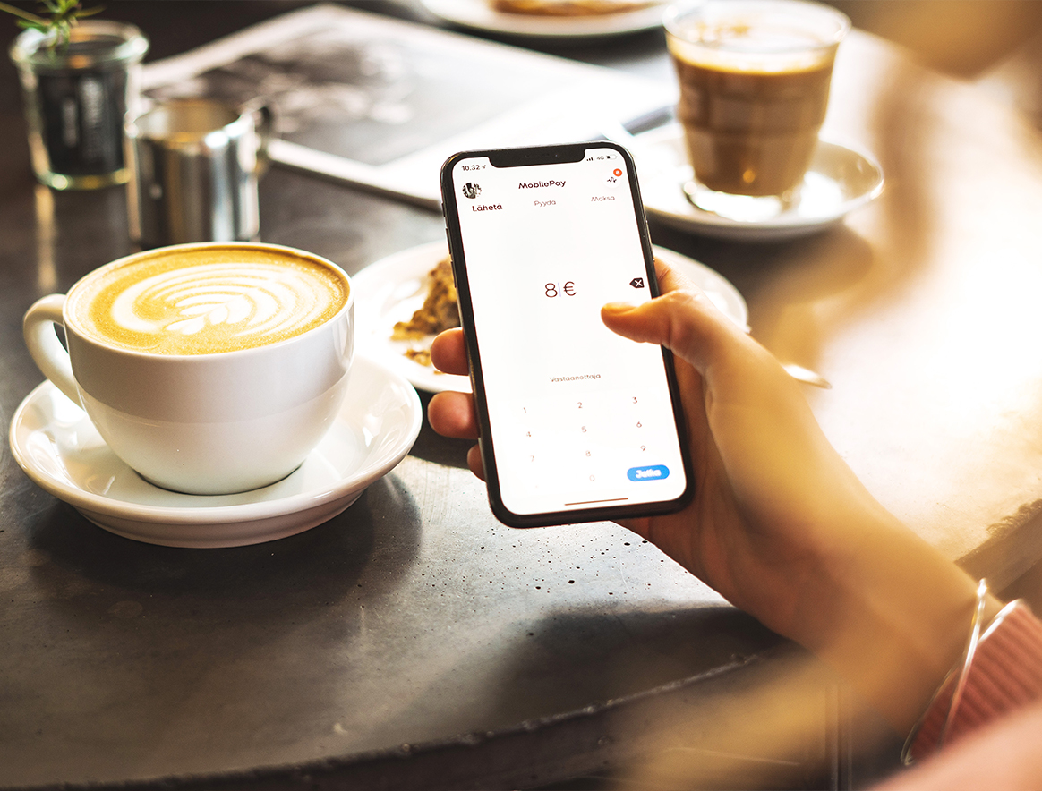 Nainen kahvilassa kahvikupin ääressä lähettämä kaverille rahaa MobilePaylla